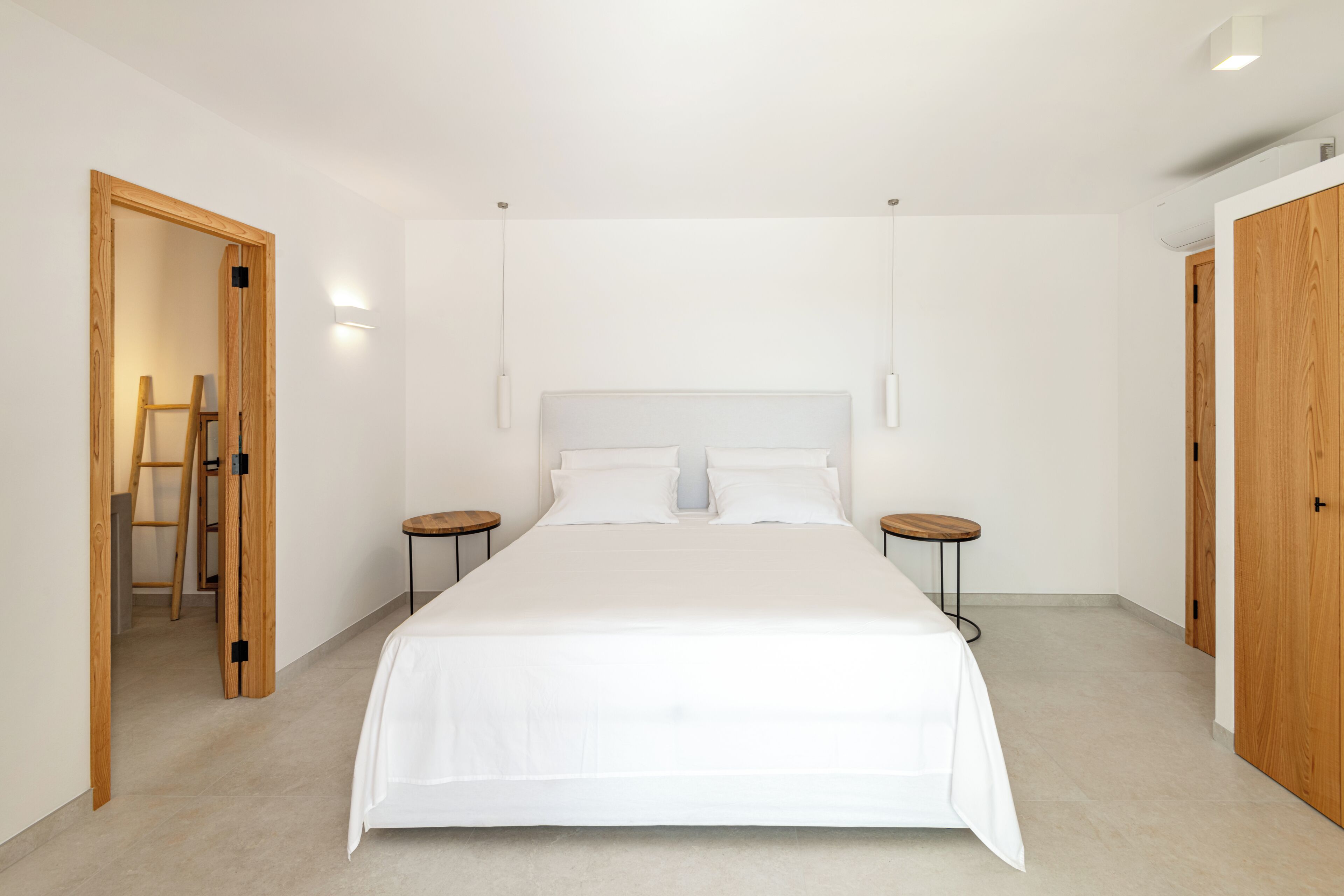 A bedroom with a large bed, two bedside tables, a ladder, and wooden doors.