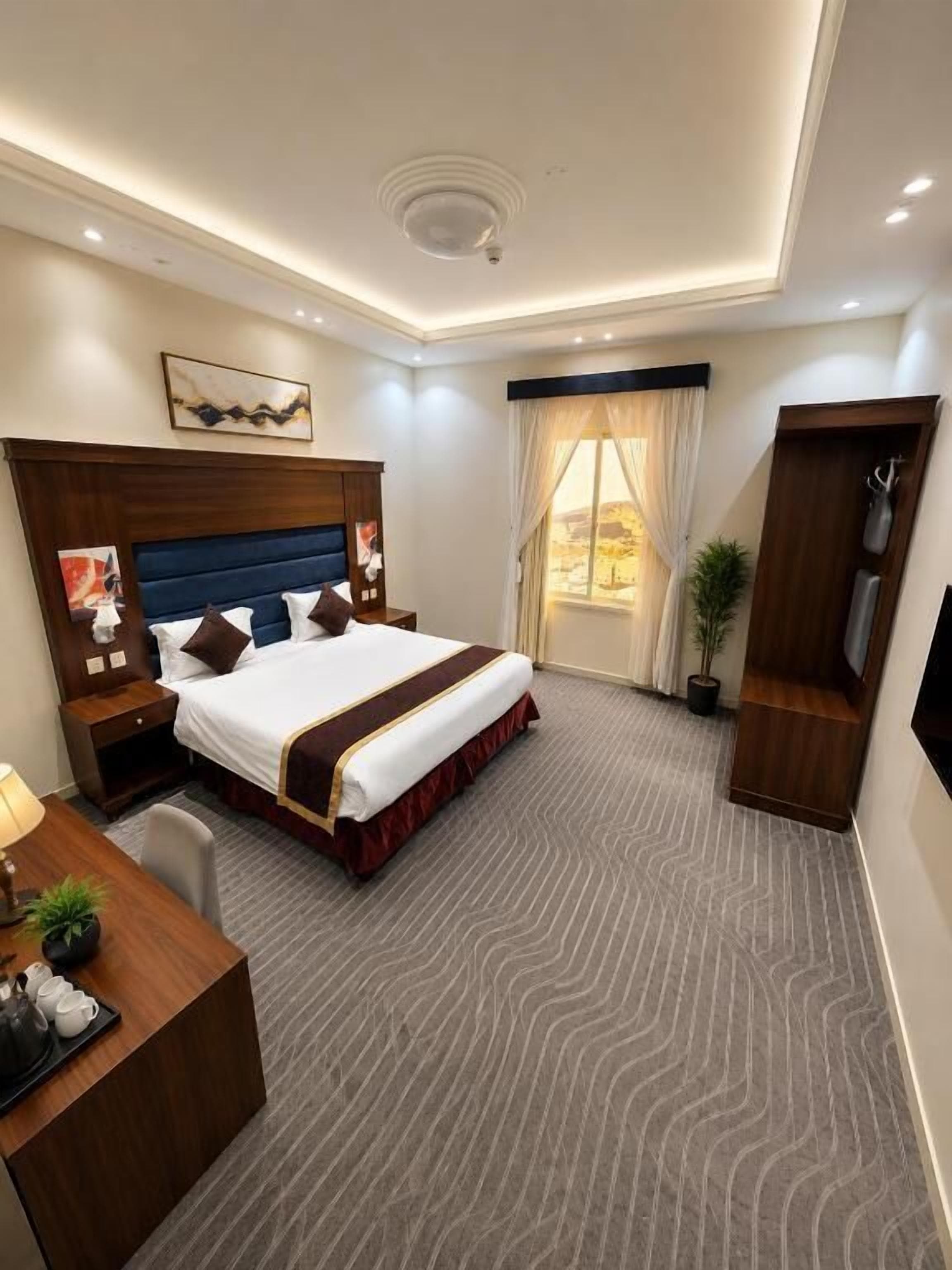 Ein Hotelzimmer mit einem großen Bett, einem Schreibtisch mit Stuhl, einem Fernseher und einem Fenster mit Vorhängen.