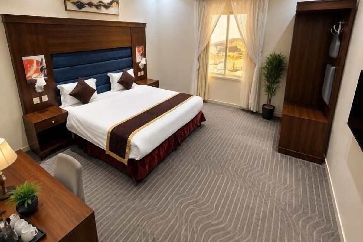 A hotel room with a large bed, a desk with a chair, a TV, and a window with curtains.