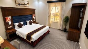 Ein Hotelzimmer mit einem großen Bett, einem Schreibtisch mit Stuhl, einem Fernseher und einem Fenster mit Vorhängen.