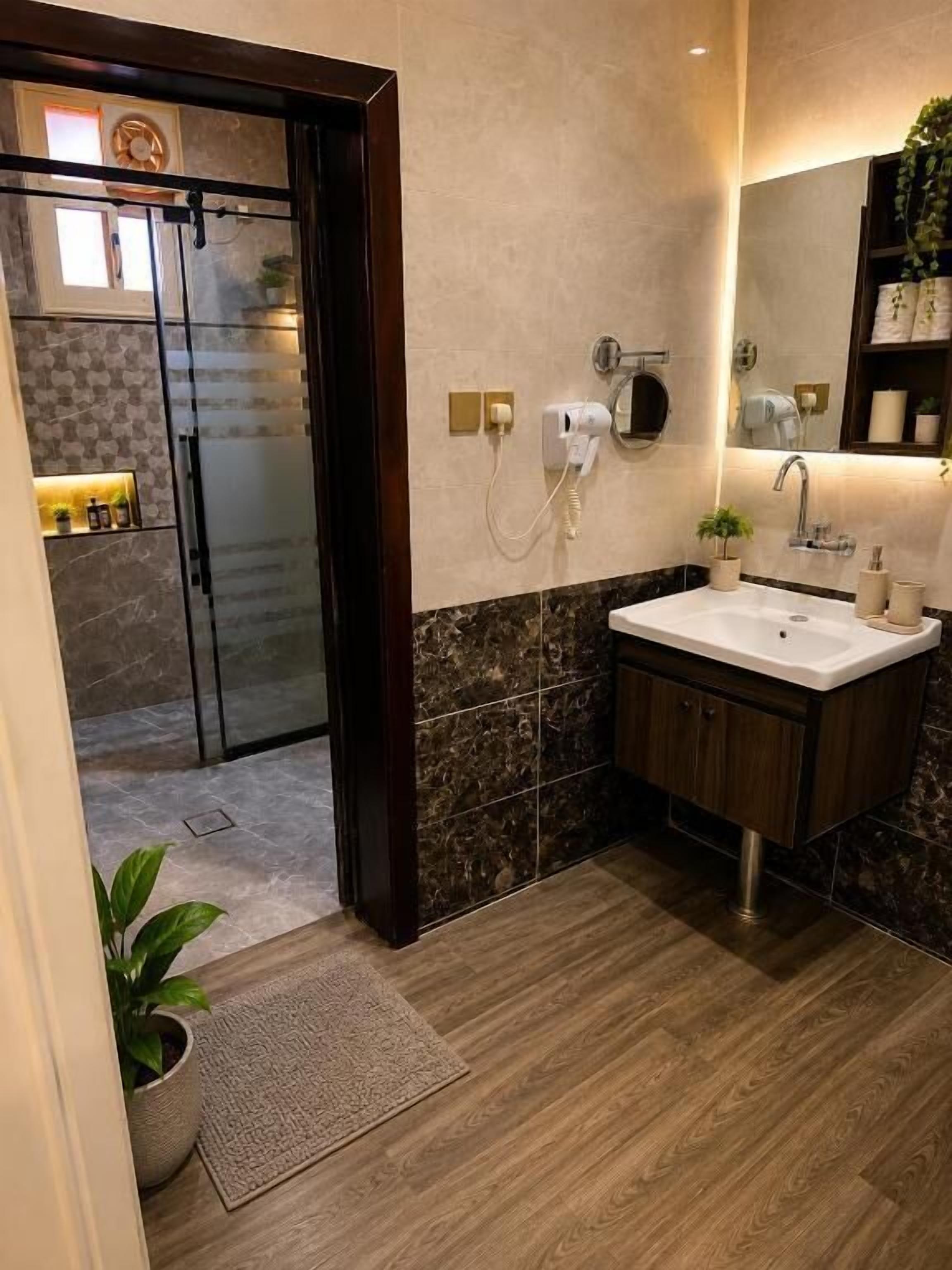 A modern bathroom with a glass shower enclosure, a sink with a mirror, and a wooden floor.