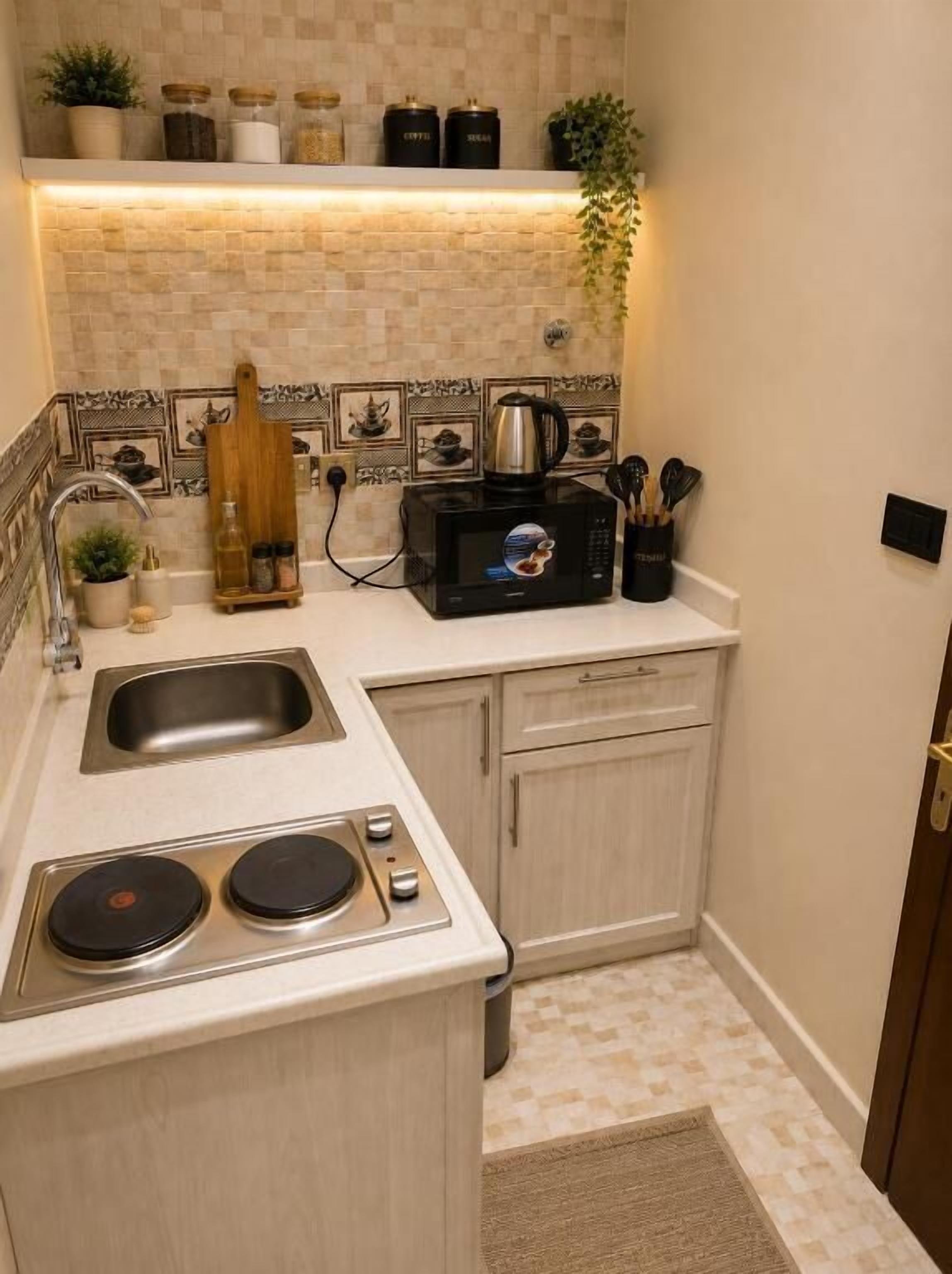 Una cucina compatta con forno a microonde, lavello e piano cottura, caratterizzata da una parete di fondo rivestita in piastrelle e mobili in legno.