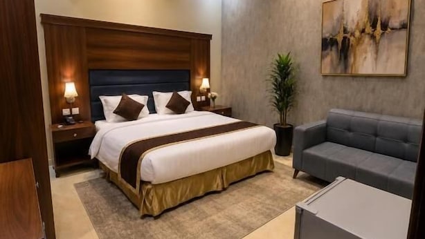Una habitación de hotel moderna con una cama grande, mesitas de noche, un sofá y un cuadro en la pared.