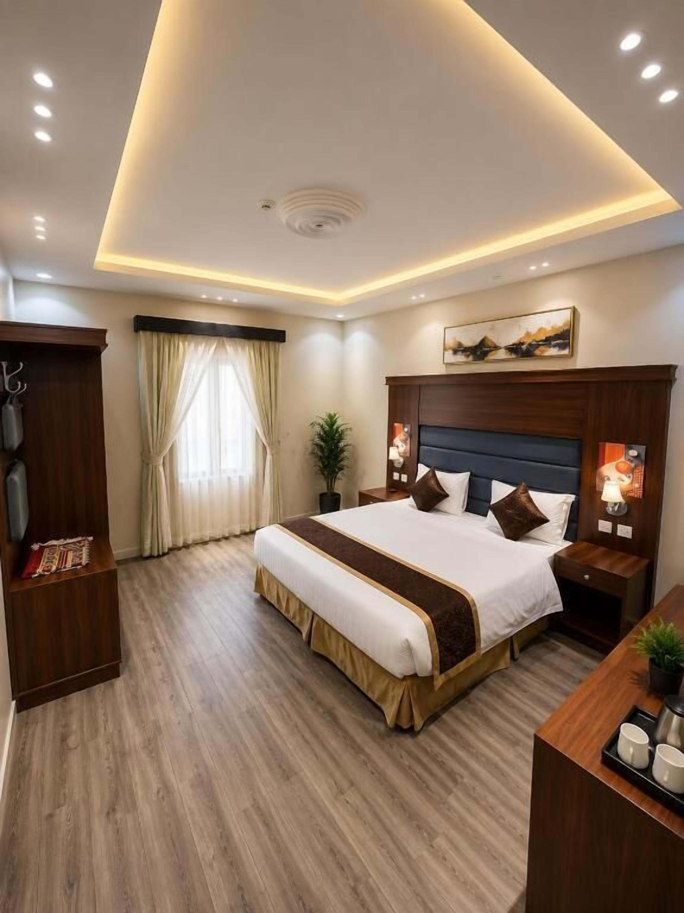 A hotel room with a large bed, bedside tables, a desk, and a ceiling light fixture.
