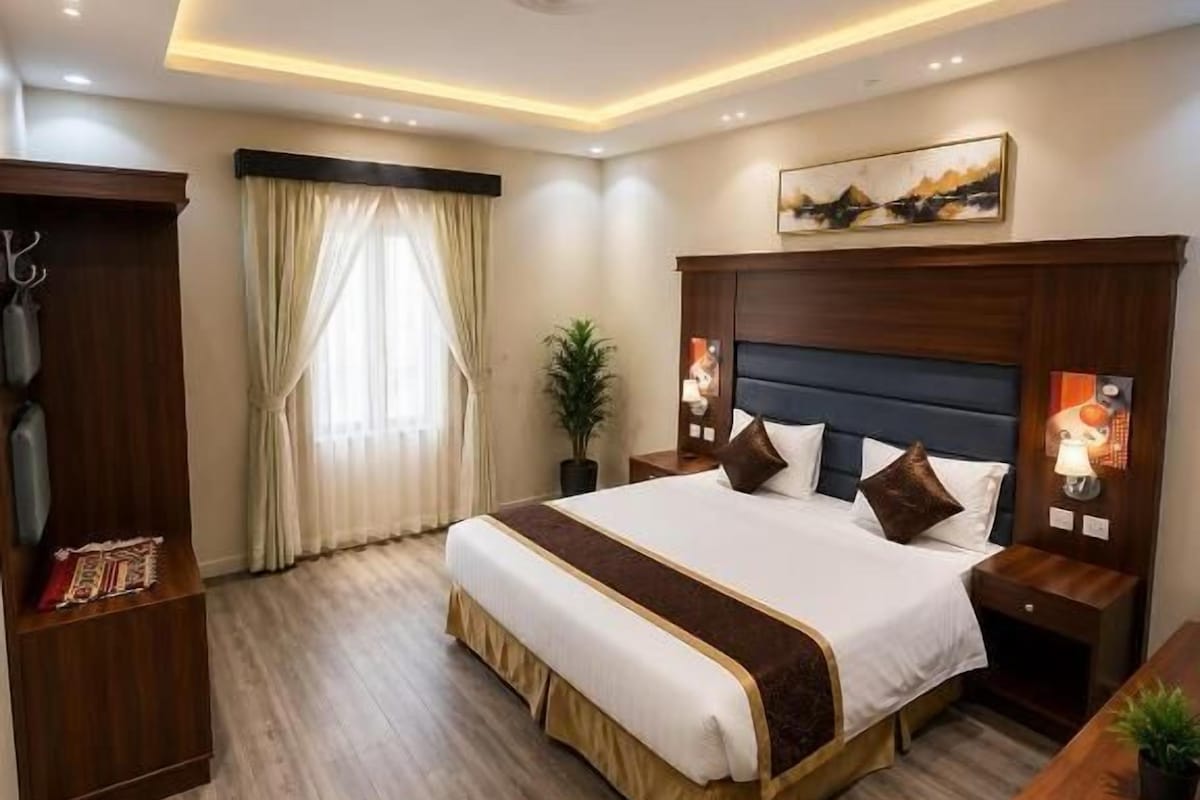 A hotel room with a large bed, bedside tables, a desk, and a ceiling light fixture.