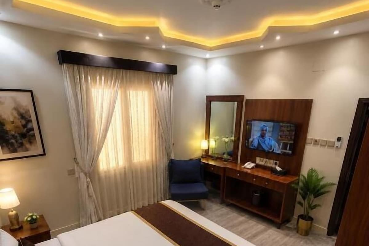 A hotel room with a large bed, a TV, a desk, and a mirror.