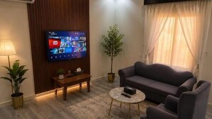 Una sala de estar moderna con un televisor de pantalla plana, un sofá, una mesa de centro y una planta en maceta.
