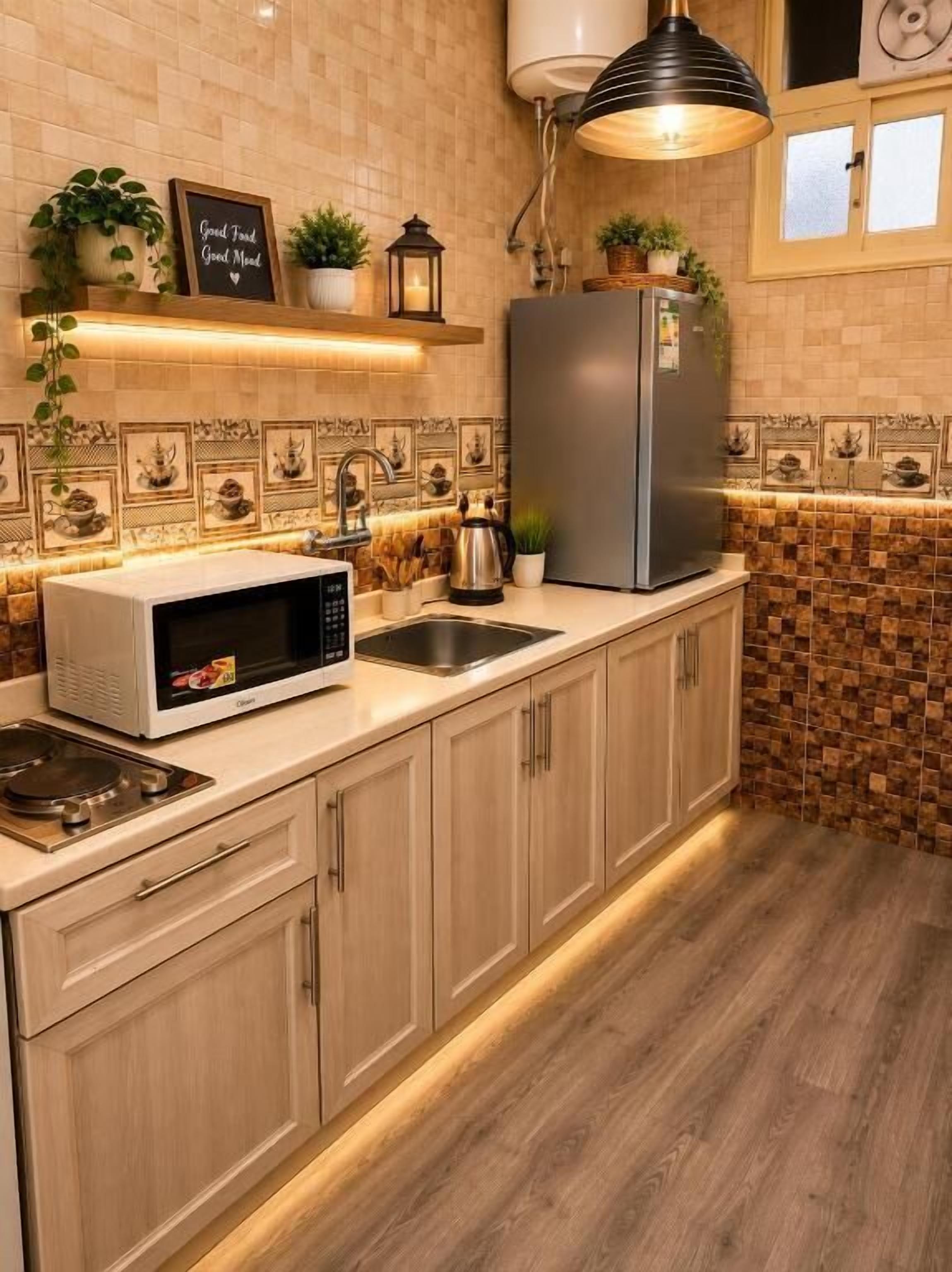 A kitchen with a microwave, sink, and stainless steel refrigerator. There are plants on the counter and a shelf above the microwave.