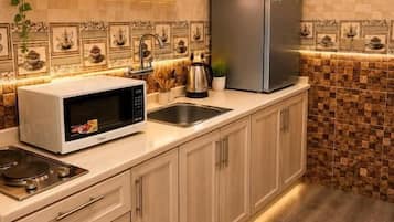 A kitchen with a microwave, sink, and stainless steel refrigerator. There are plants on the counter and a shelf above the microwave.