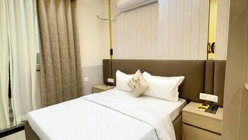 Habitación de hotel moderna con una cama grande, una mesita de noche con lámpara, un equipo de aire acondicionado y un ventilador de techo.
