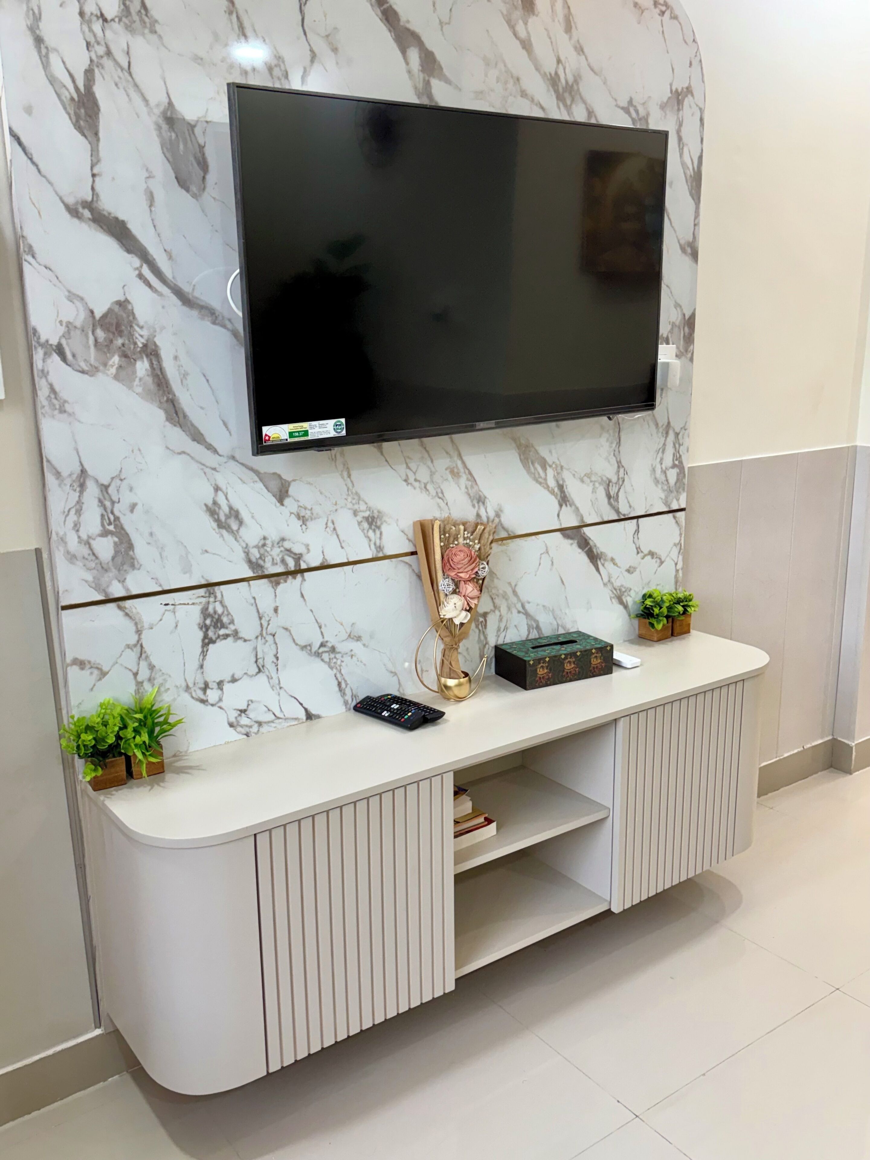 Un mueble moderno para entretenimiento con un televisor de pantalla plana montado en una pared de mármol, un jarrón decorativo y una planta pequeña en la consola.