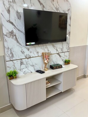 A modern entertainment unit with a flat-screen TV mounted on a marble wall, a decorative vase, and a small plant on the console.