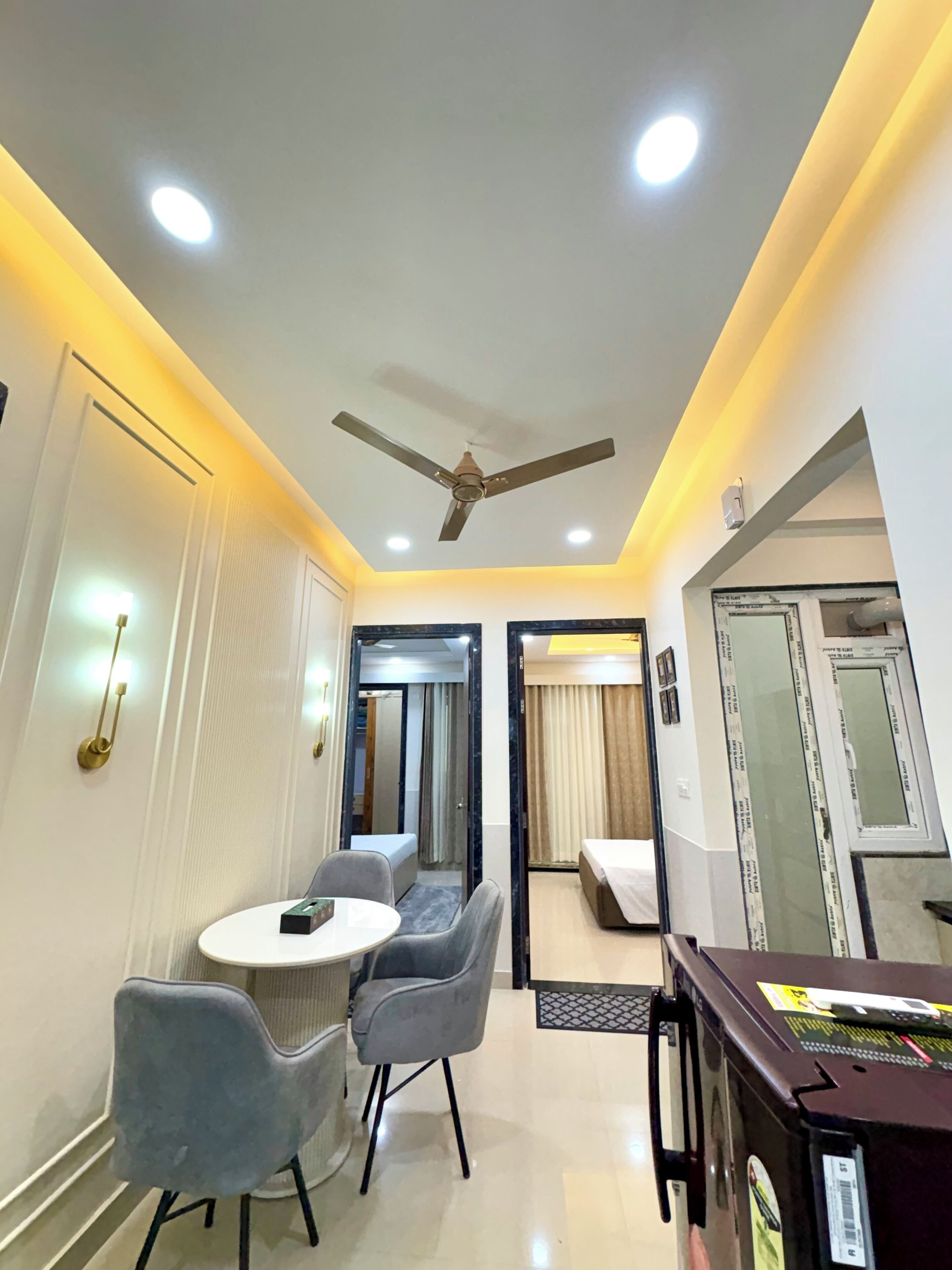 A hotel room with a ceiling fan, a round dining table with two chairs, a bed, and a large mirror.