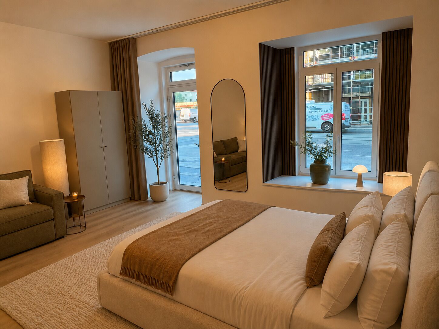 Habitación de hotel con cama, sofá, armario, espejo y ventana con vista a la calle.