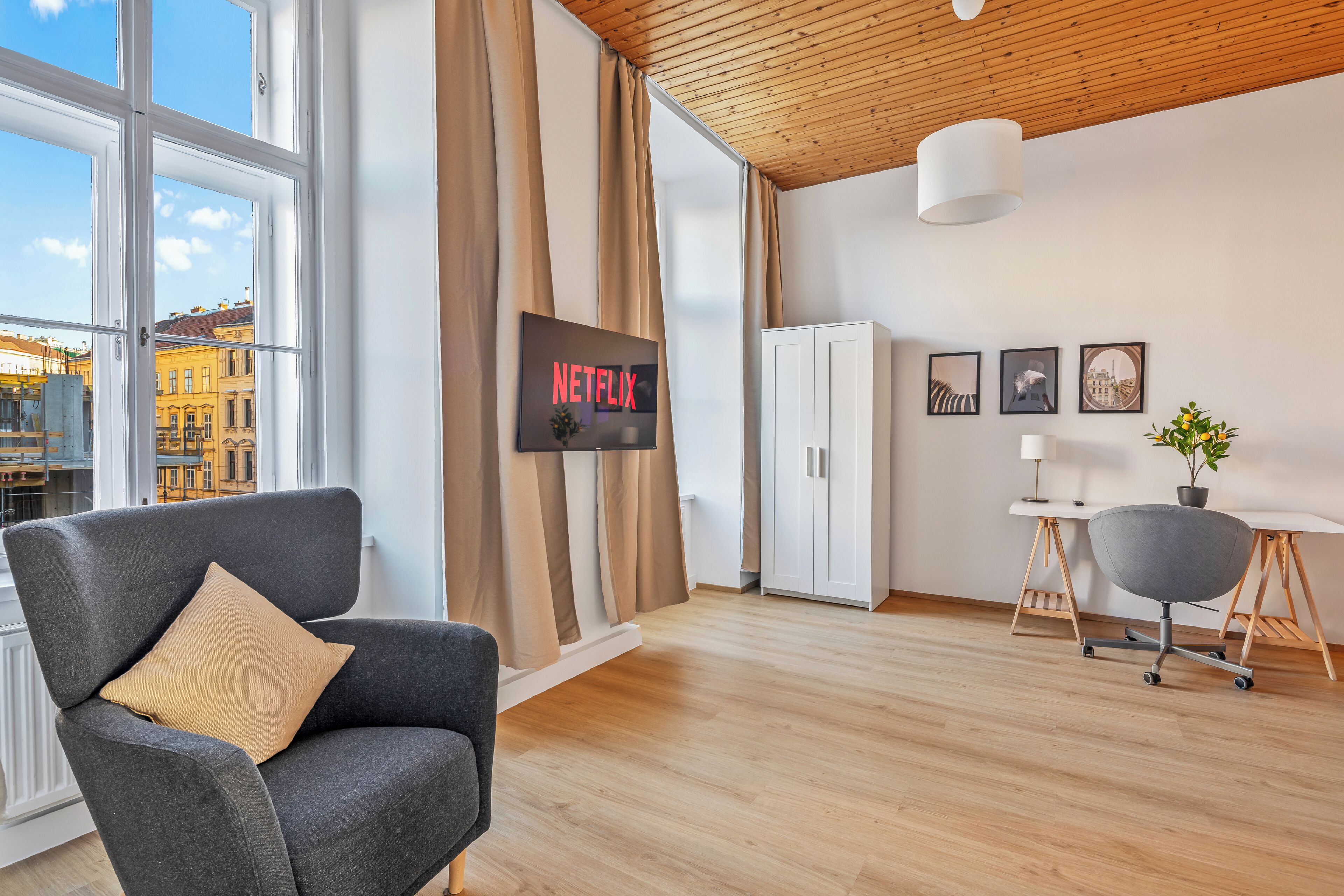 A modern living room with a large window, a sofa, a cabinet, and a desk with a lamp.