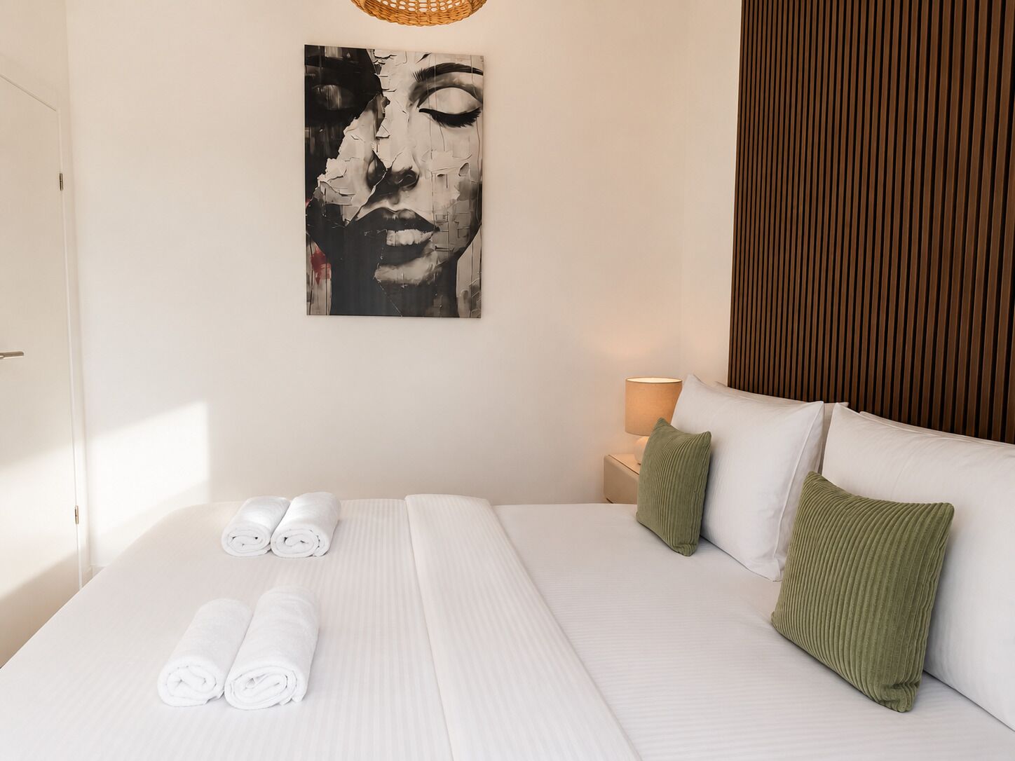 A hotel room with a bed, pillows, a wall art piece, a nightstand, and rolled towels.