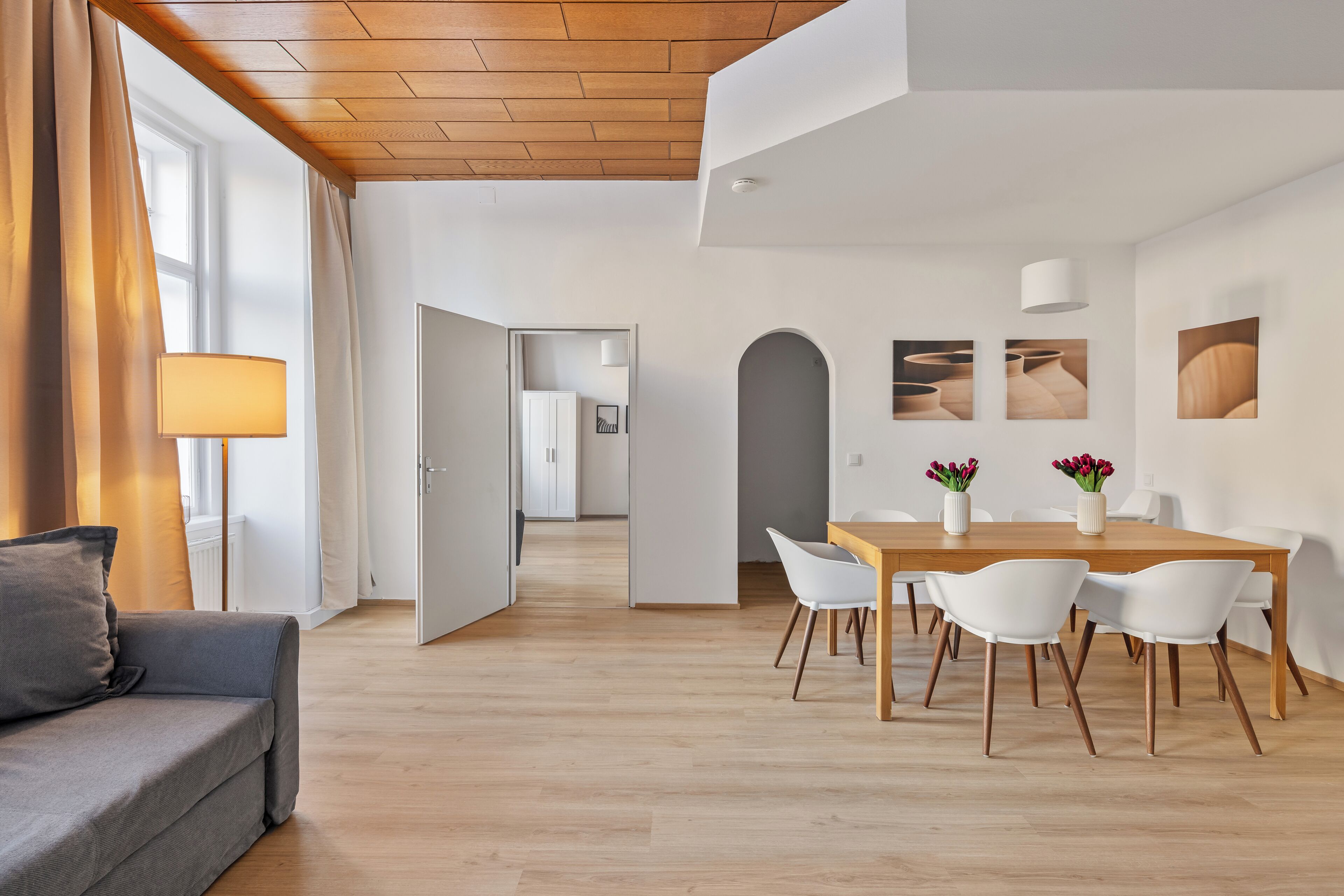 A modern living room with a sofa, a dining area with a table and chairs, and a hallway leading to another room.