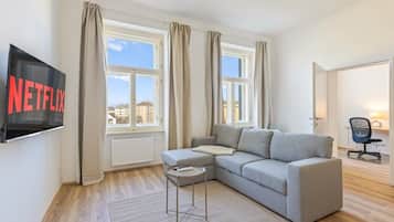 Una sala de estar moderna con un sofá gris, una mesita auxiliar, un televisor de pantalla plana montado en la pared y una ventana con cortinas.
