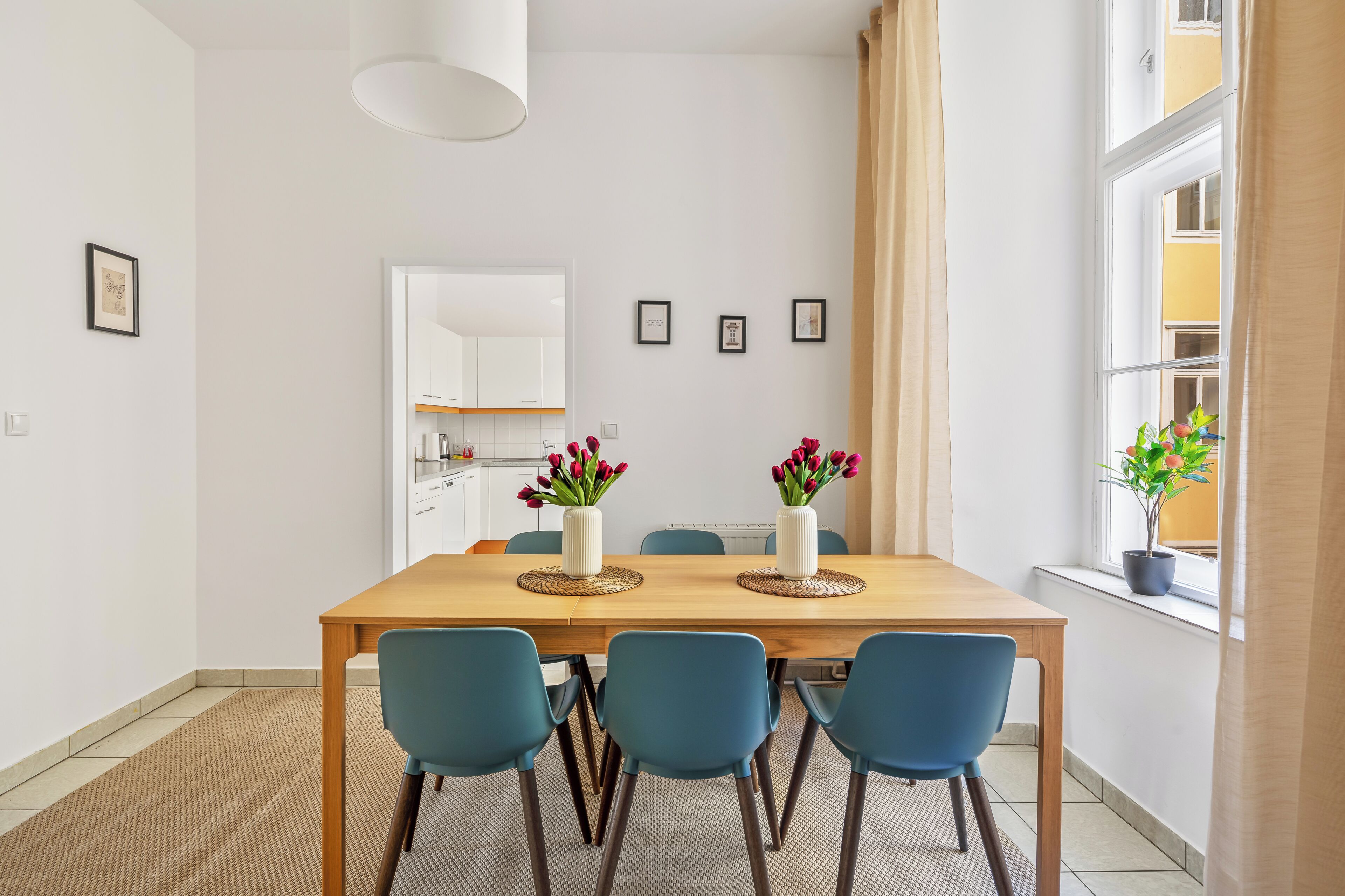 Un comedor con una mesa de madera, sillas azules y dos jarrones con flores rojas.