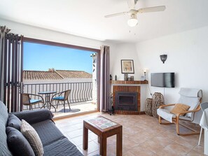 Ein Wohnzimmer mit Sofa, Tisch, Kamin, Fernseher und einem Balkon mit Dachblick.