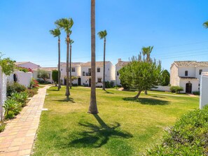 A courtyard with palm trees, a paved walkway, and white buildings with tiled roofs. - Los Naranjos 11B Capistrano Village by Casasol by Interhome (Nerja)