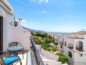 A balcony with a table and chairs, overlooking a coastal town with buildings and a clear sky. - Los Naranjos 11B Capistrano Village by Casasol by Interhome (Nerja)