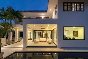 A modern house with a glass facade, a balcony, and a dining area with a ceiling fan. - Spacious 4-bedroom Mansion with indoor pool table near Hua Hin City (Tambon Hua Hin)