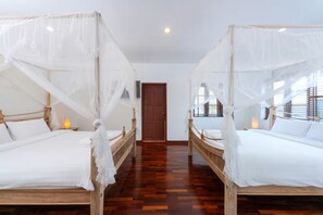 Ett hotellrum med två sängar, var och en med ett himmelssängsöverdrag, trägavlar och vitt sänglinne.