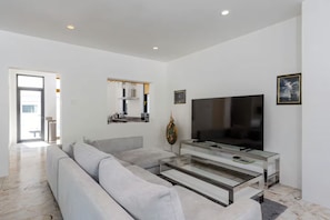 A modern living room with a grey sofa, a glass coffee table, a flat-screen TV, and a fireplace. - Spacious 4-bedroom Mansion with indoor pool table near Hua Hin City (Tambon Hua Hin)