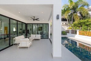A modern interior with glass walls, a ceiling fan, and a poolside area with outdoor furniture. - Spacious 4-bedroom Mansion with indoor pool table near Hua Hin City (Tambon Hua Hin)