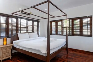 A four-poster bed with white linens, a bedside table with a lamp, and wooden blinds on windows. - Spacious 4-bedroom Mansion with indoor pool table near Hua Hin City (Tambon Hua Hin)