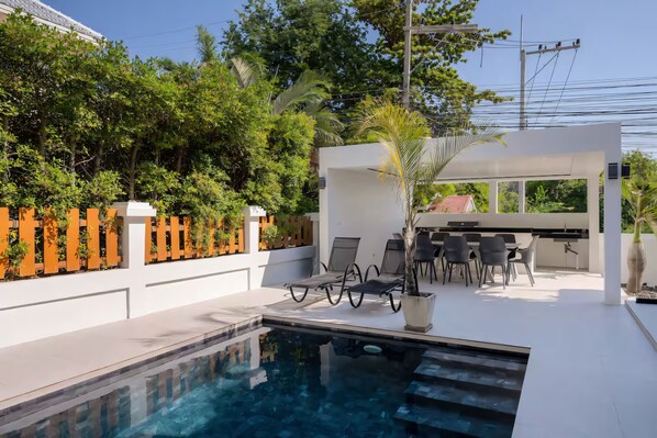 A modern outdoor pool area with lounge chairs, a dining table, and a pergola. - Spacious 4-bedroom Mansion with indoor pool table near Hua Hin City (Tambon Hua Hin)