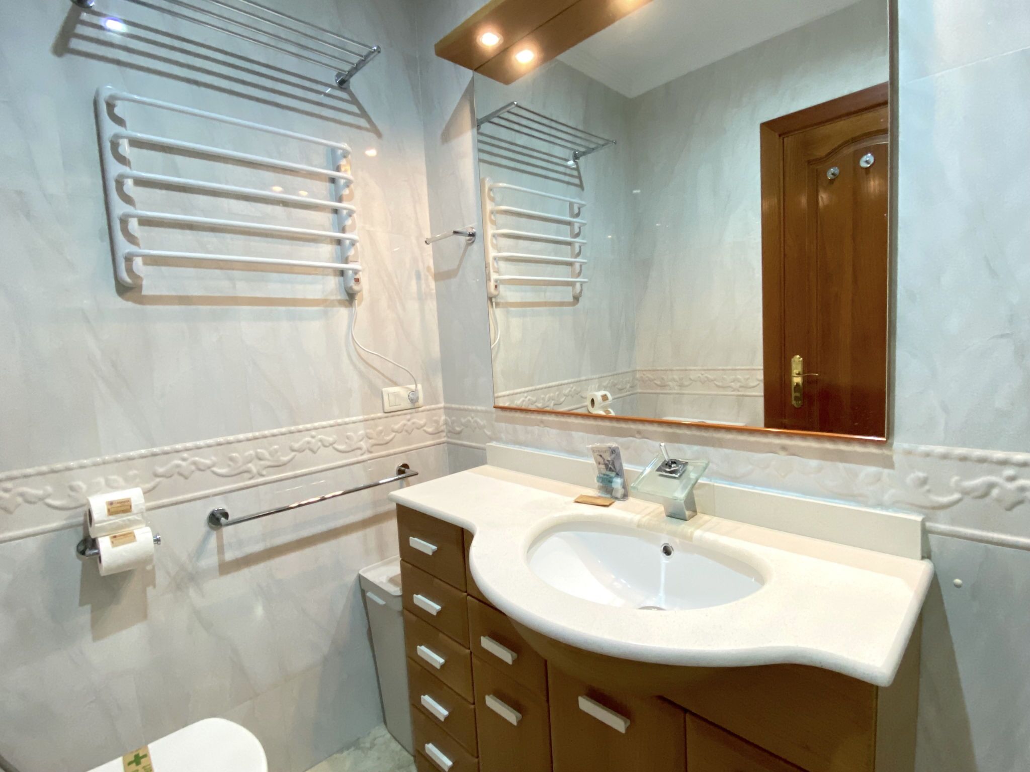 Ein Badezimmer mit Waschbecken, Spiegel, Handtuchhaltern und Toilette.