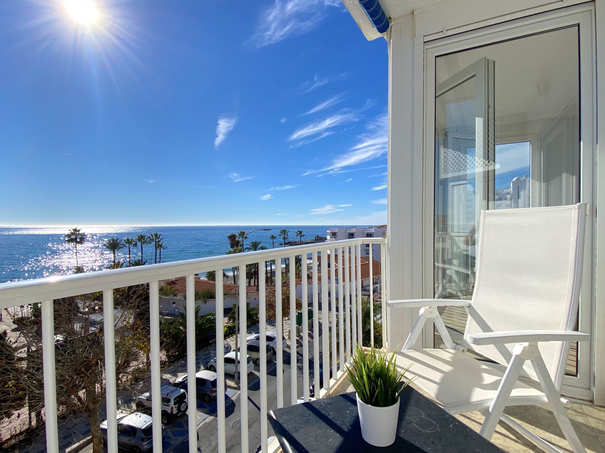 A balcony with a view of the ocean, a white chair, and a potted plant.