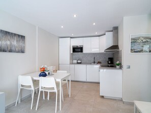 A modern kitchen with white cabinets, a dining table with chairs, and a small island. - Capuchinos 48 San Juan Capistrano by Casasol by Interhome (Nerja)