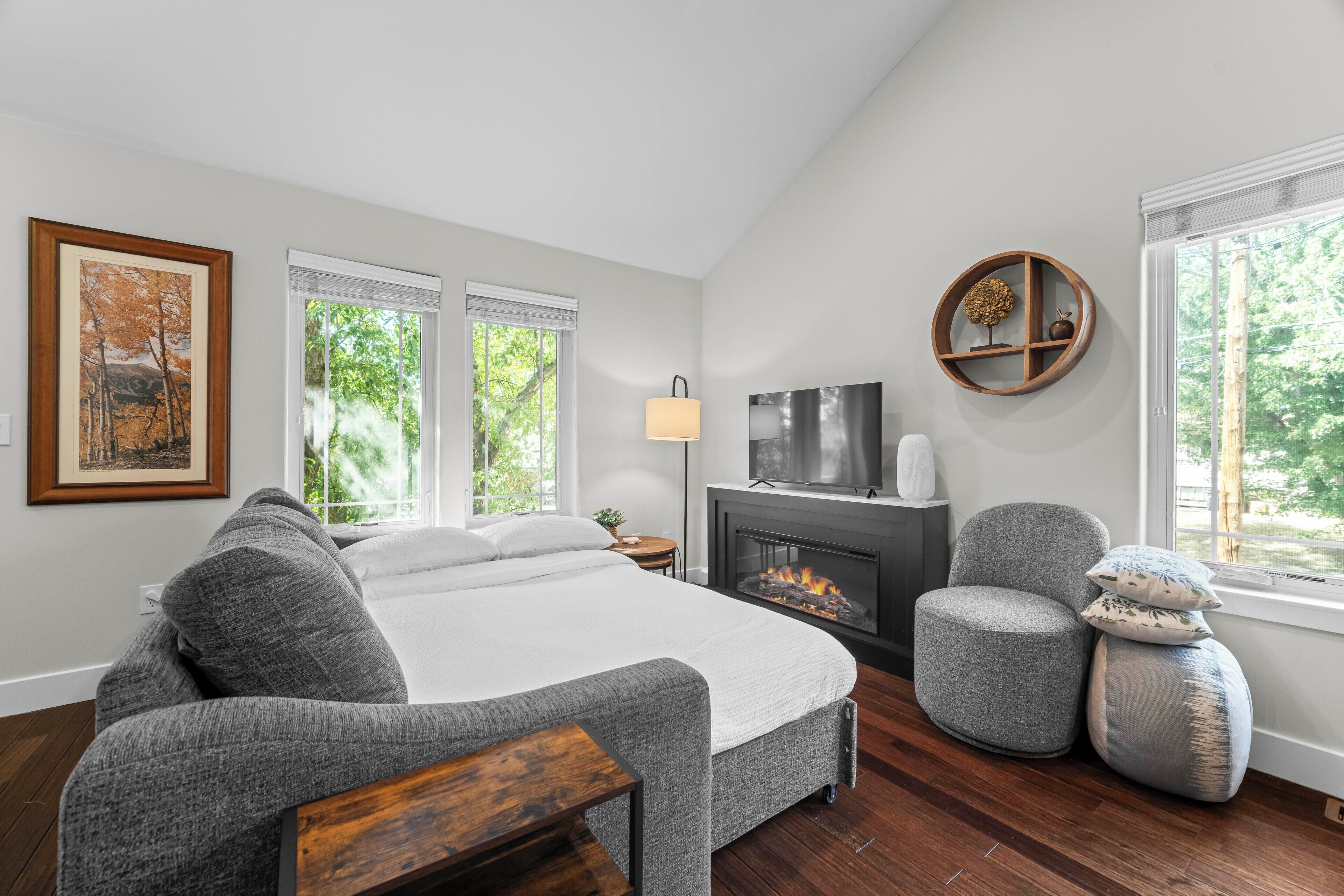 Un dormitorio con cama, televisor, chimenea y ventana con vista a árboles.