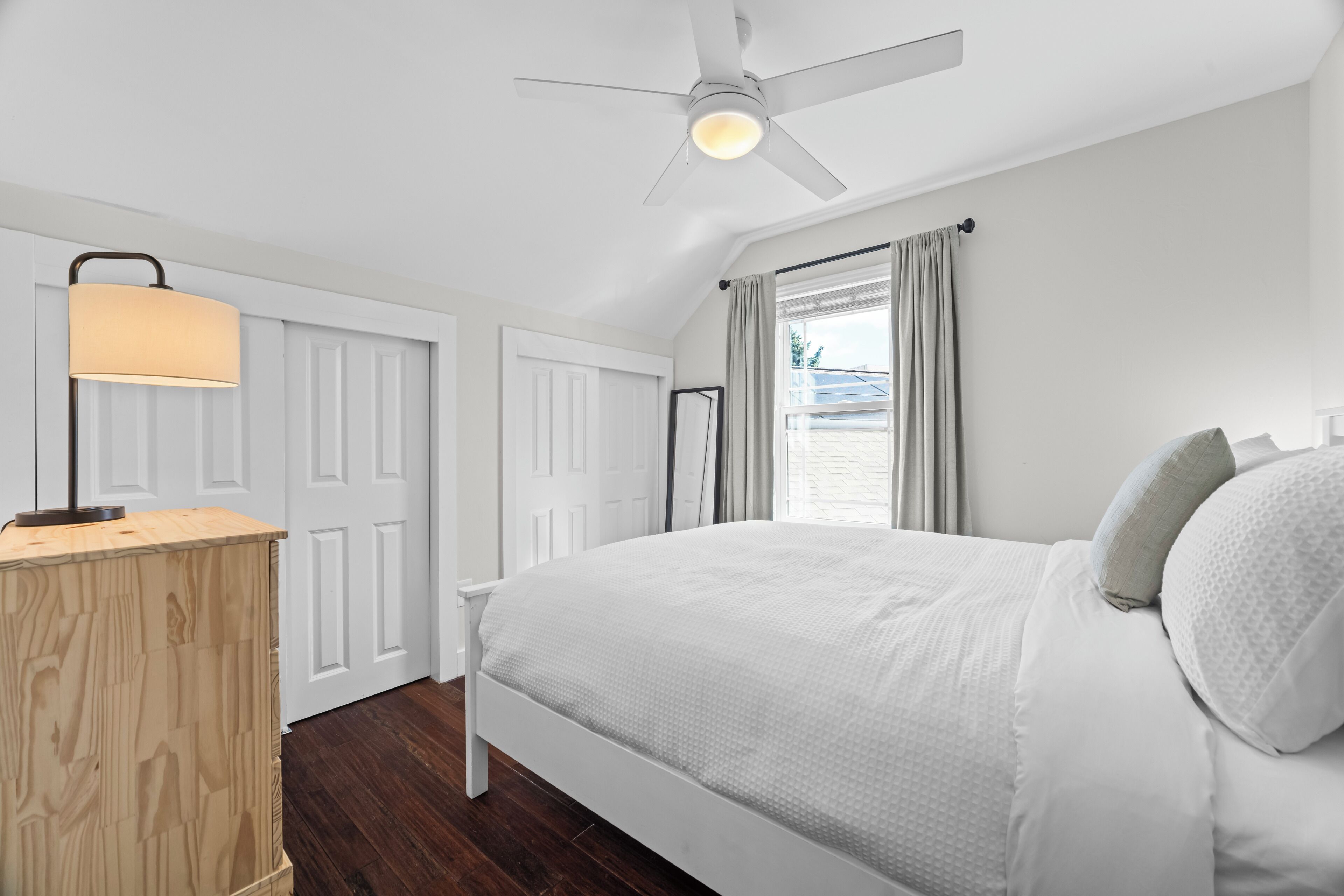 A bedroom with a bed, a desk, a ceiling fan, and a window with curtains.