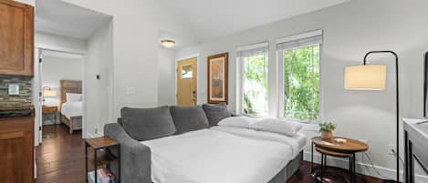 A bedroom with a bed, a bedside table, a lamp, and a view of the outdoors through the windows.