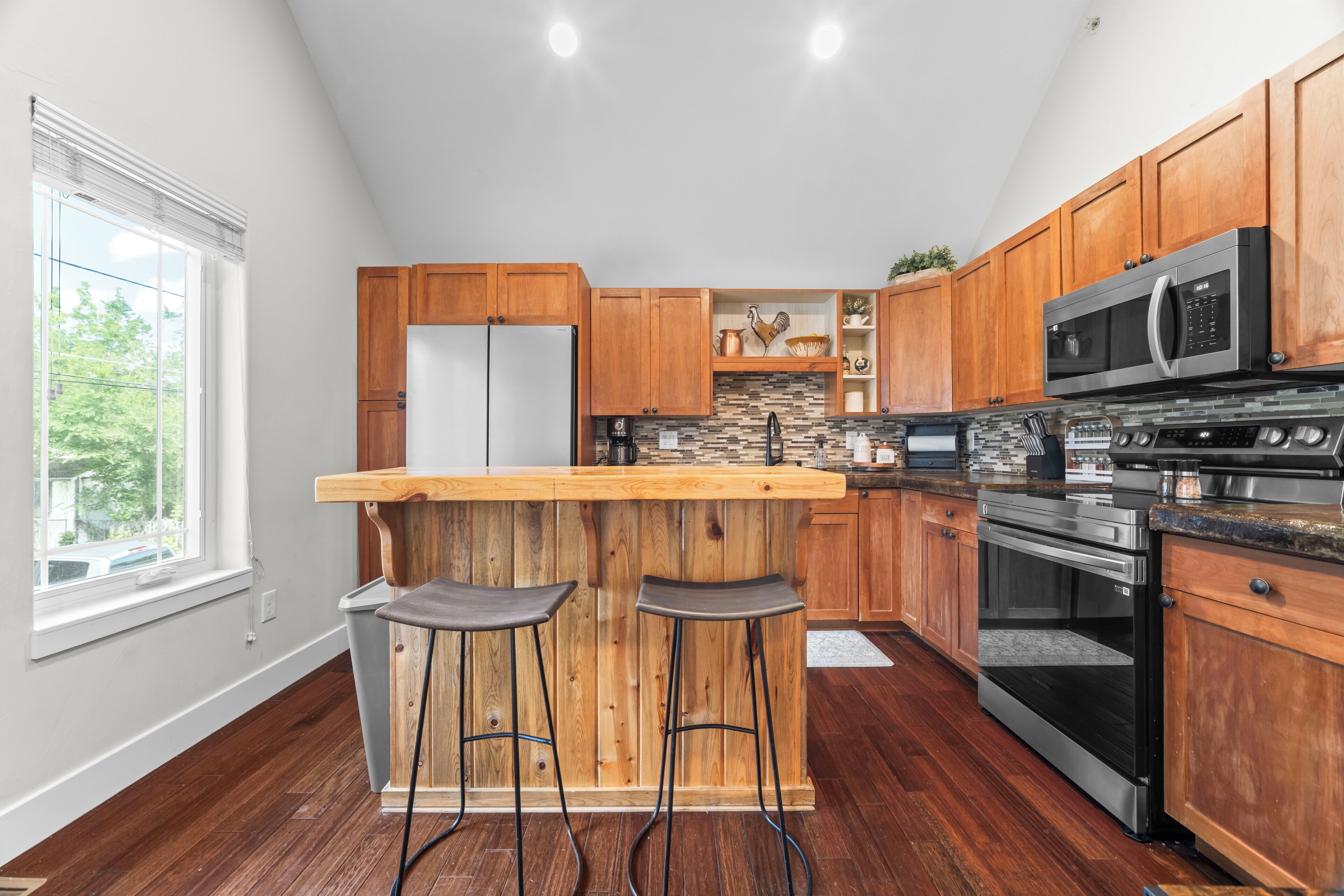 Una cocina moderna con armarios de madera, un refrigerador de acero inoxidable, un horno empotrado y una zona de bar con taburetes.