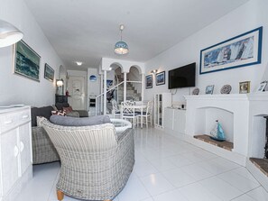 A spacious living area with a wicker sofa, a dining table with chairs, a fireplace, and a TV mounted on the wall. - Los Pinos 29 Villas by Casasol by Interhome (Nerja)