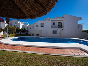 Un edificio residencial con piscina, paredes blancas y techo de paja.