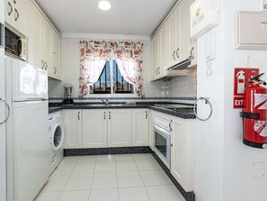 A kitchen with white cabinets, a washing machine, a microwave, and a fire extinguisher. - Los Pinos 29 Villas by Casasol by Interhome (Nerja)