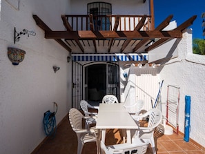 Een terras met een tafel en stoelen, een pergola en een poort naar een binnenruimte.