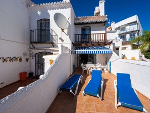 A white building with a terrace, blue lounge chairs, and a striped awning. - Los Pinos 29 Villas by Casasol by Interhome (Nerja)
