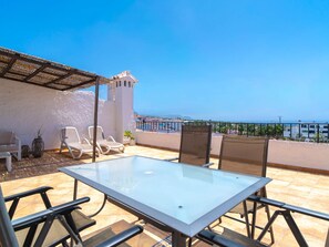 Une terrasse avec une table et des chaises, un mur blanc et une vue sur la mer.