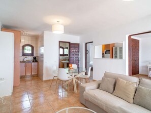 A modern living room with a sofa, a glass dining table with chairs, a kitchen in the background, and a bathroom visible through an open door. - Capistrano Village Pueblo 15 by Casasol by Interhome (Nerja)