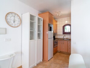 Une cuisine compacte avec des meubles blancs, un four encastré et une horloge au mur.