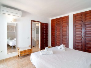 A hotel room with a bed, a wooden wardrobe, a wooden chair, a small table, and a bathroom visible through an open door. - Capistrano Village Pueblo 15 by Casasol by Interhome (Nerja)