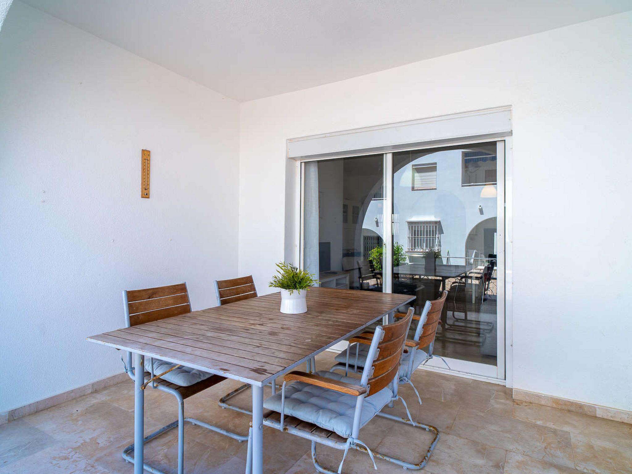 Un coin repas avec une table en bois et des chaises en métal, une plante en pot et une porte-fenêtre coulissante donnant sur un espace extérieur.