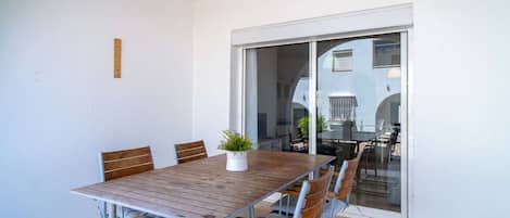 Un coin repas avec une table en bois et des chaises en métal, une plante en pot et une porte-fenêtre coulissante donnant sur un espace extérieur.